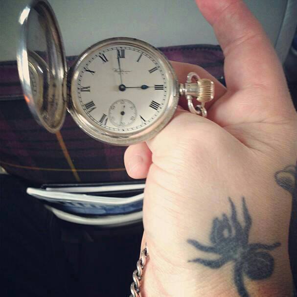 An open silver pocket watch held in a hand.